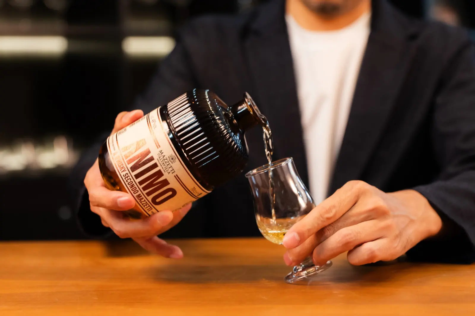 Close-up of hands pouring ANIMO whisky into a tasting glass.