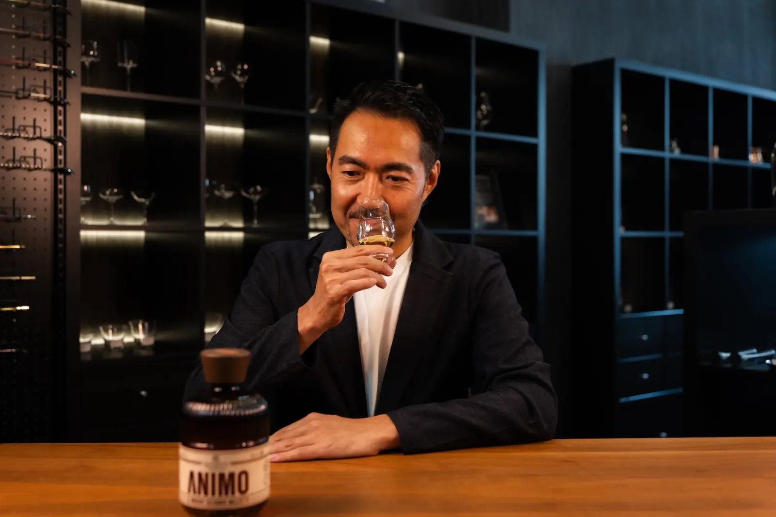 Yusuke Nomiya smelling a drink in a glass, with an ANIMO bottle in the foreground.