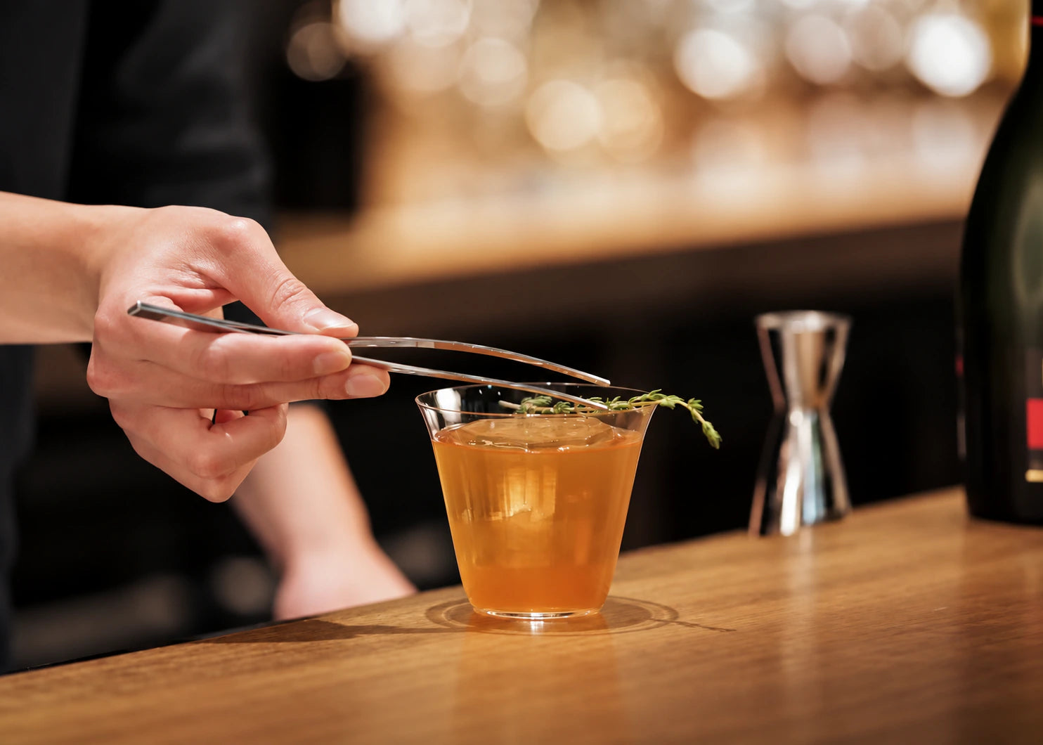 Garnishing a cocktail with herbs using tongs